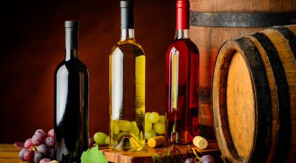Wine bottles in cellar rose, white and red wine bottles on wooden table and with barrels.
